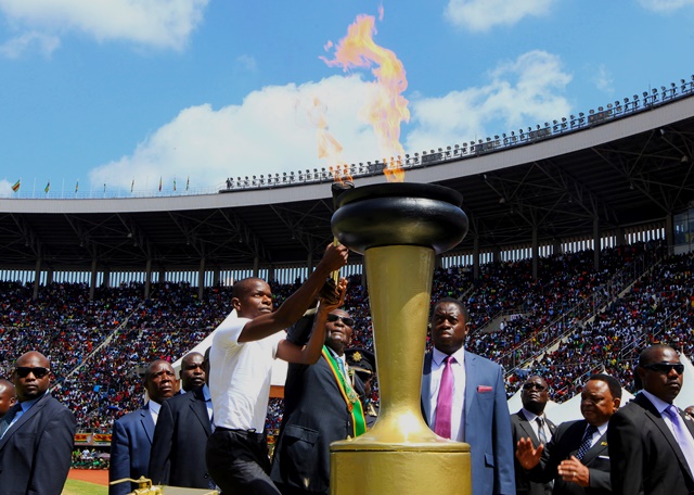 Zimbabwean President Robert Mugabe is assisted to light the anniversary flae