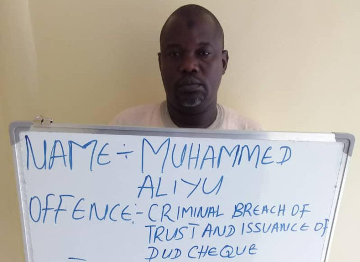 Aliyu at the court premises displaying a board stating his offence. Photo Credit: EFCC