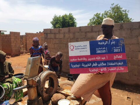 Rabiu Musa, standing and holding Signpost the Qatar Charity foundation borehole. PC: Lukman Abdulmalik